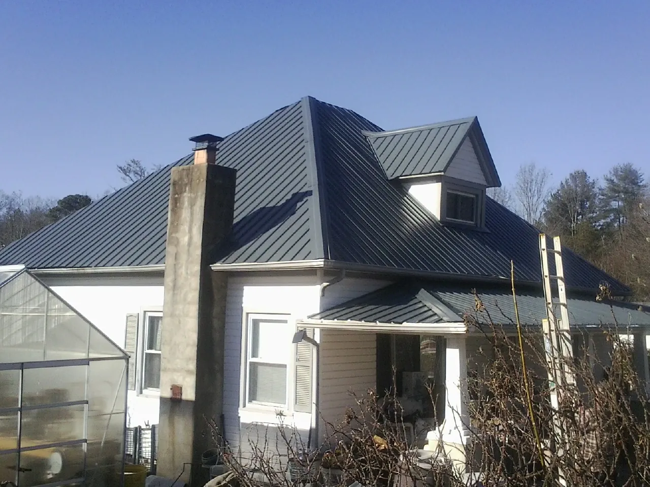 Dark blue standing seam metal roof on a white farmhouse with dormer — Slate & Tile Roof Repair by Roofing Brothers in Christine