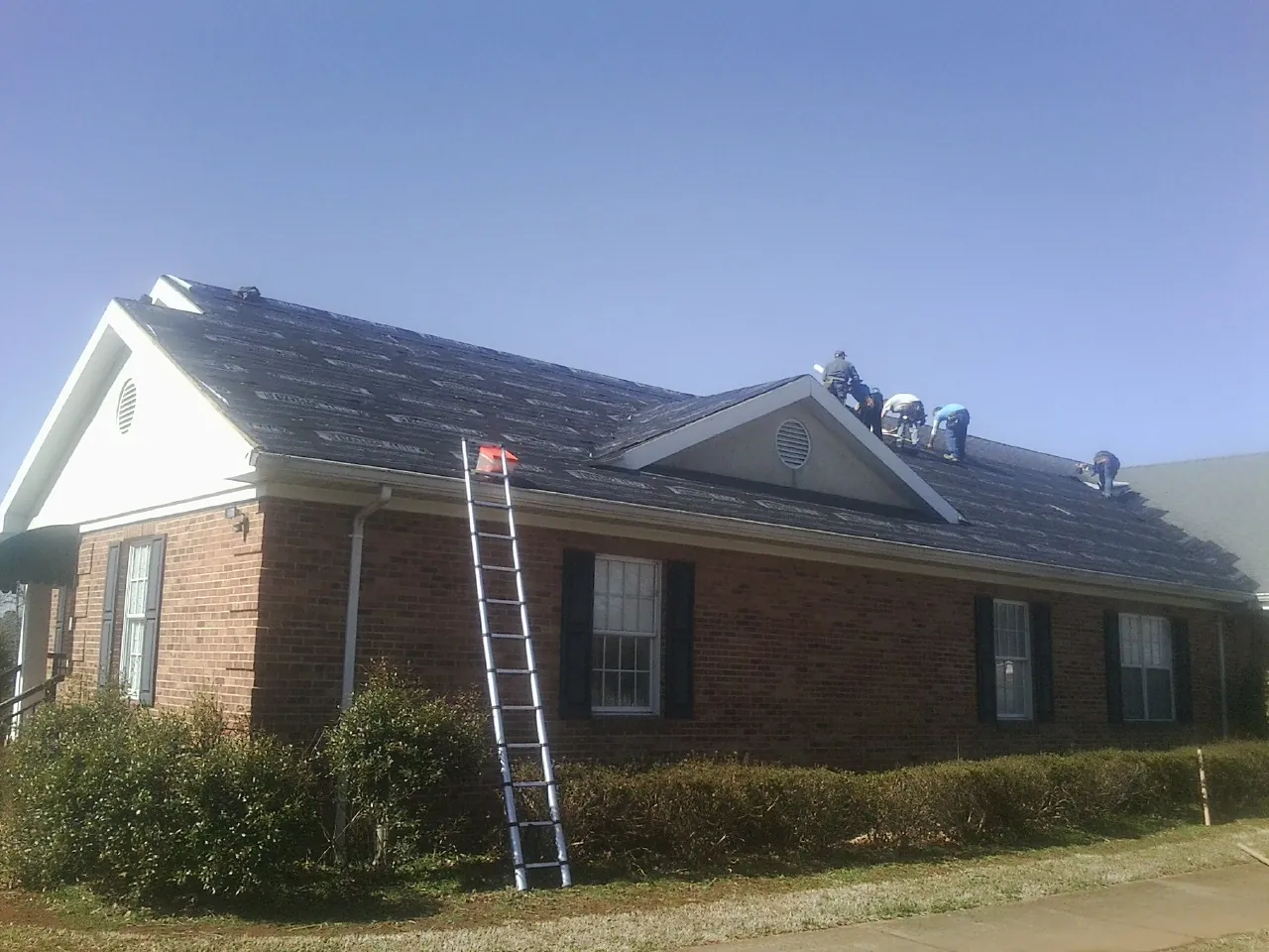 Crew tearing shingles off a brick ranch roof with a ladder set — Emergency Roof Repair work by our crew in Christine