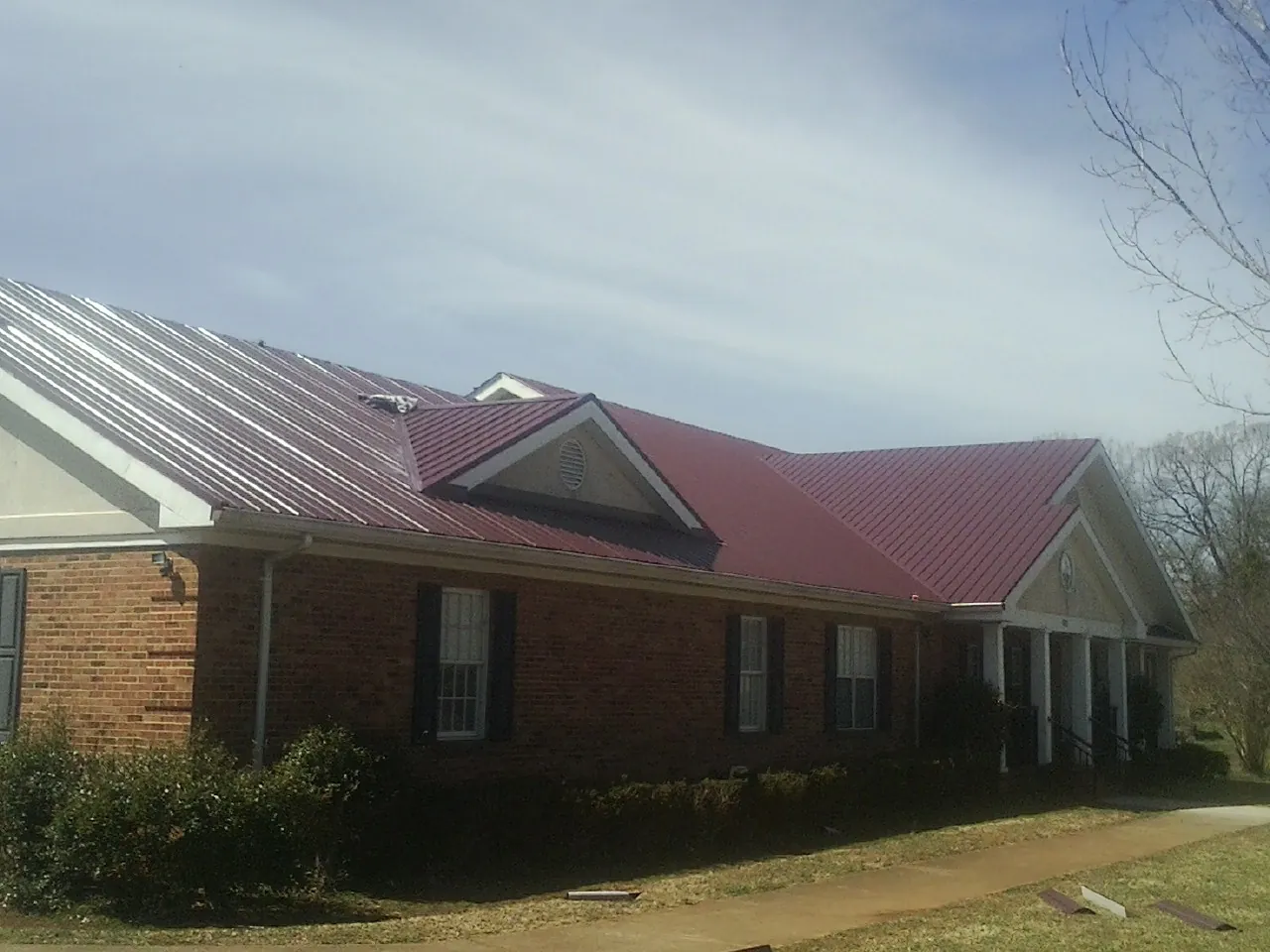 Red metal roof with gabled entries on a long brick building, from a Hail Damage Roof Repair job in Christine