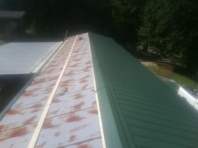 Old rusted panels beside newly installed green metal roofing — Wind Damage Roof Repair by Roofing Brothers in Christine