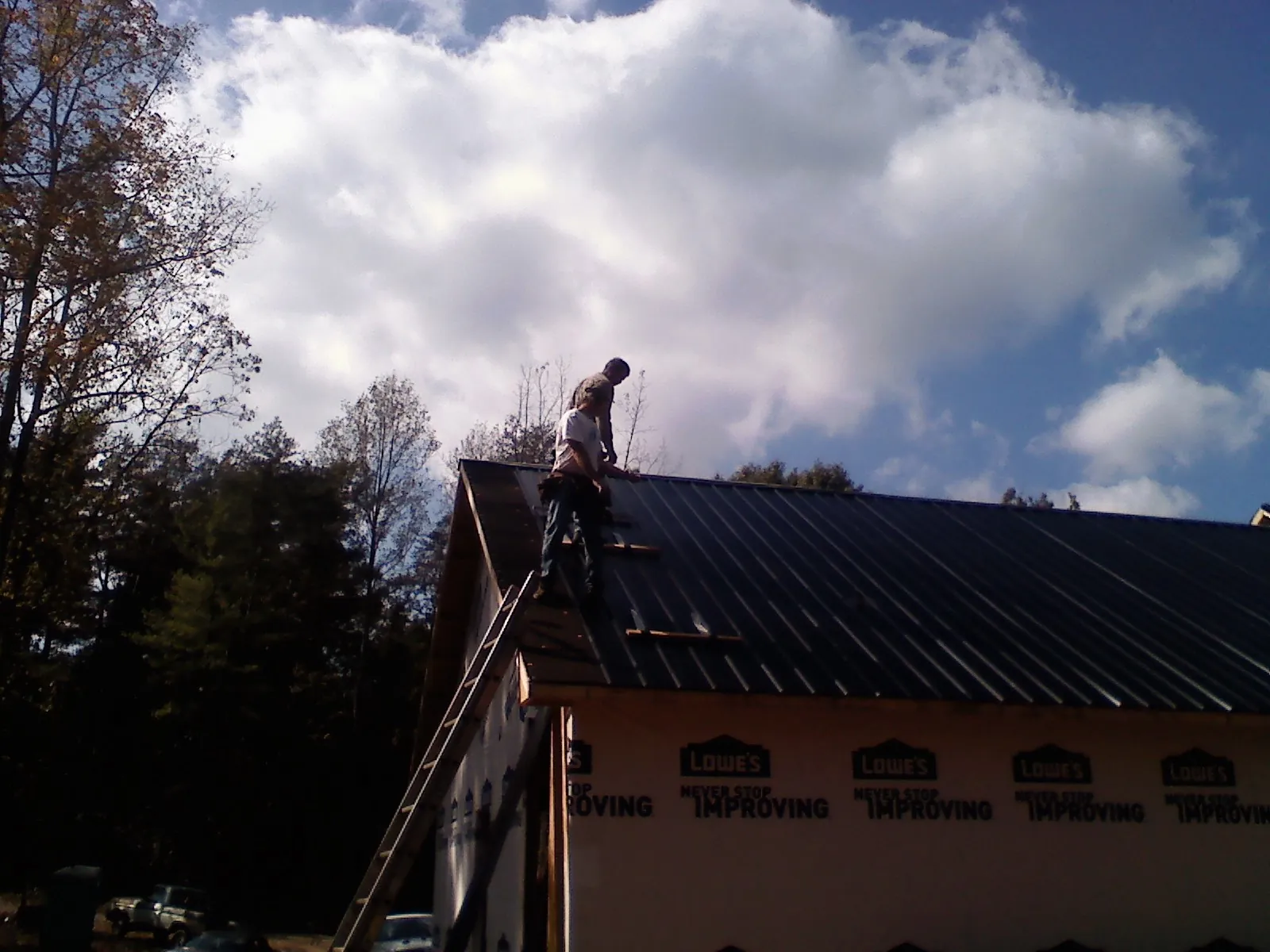 Roofer fastening dark metal panels high against a cloudy sky, from a Roof Inspection job in Christine