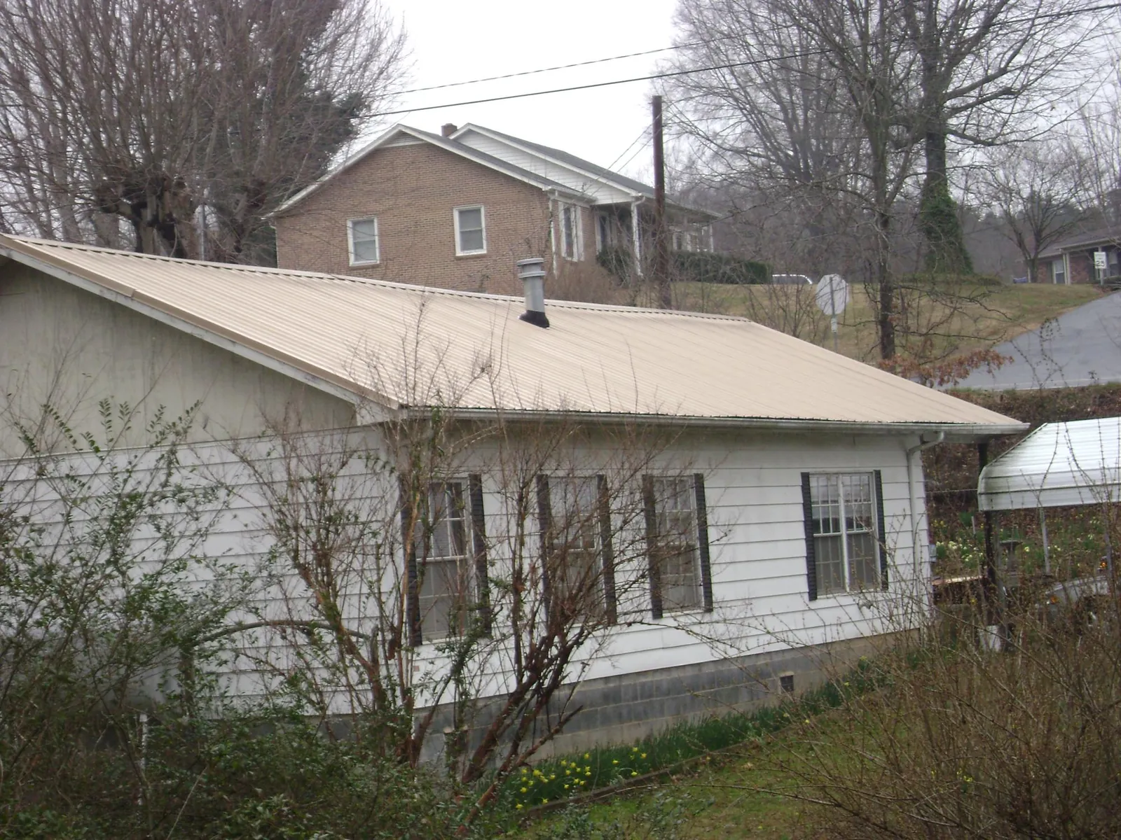 Tan metal roof on a white sided house set into a hillside — Commercial Roofing by Roofing Brothers in Christine