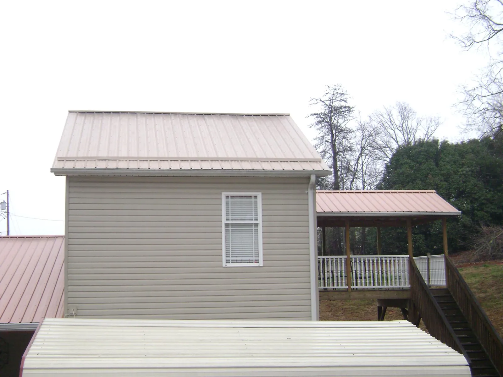 Tan metal roofs on a two story addition and attached porch, from a Roof Replacement job in Christine